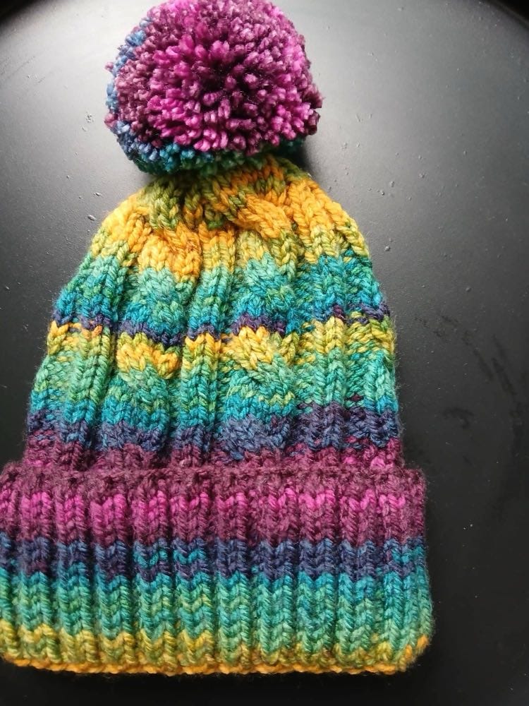 Cable-knit bobble hat striped mustard, teal, green and navy, with a plum and magenta cuff and a magenta bobble